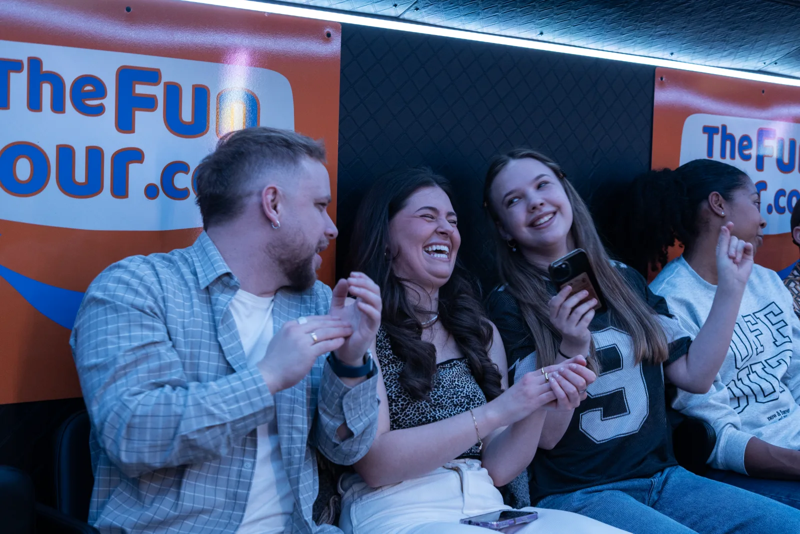 Three guests laughing together on the bus under The Fun Tour logo
